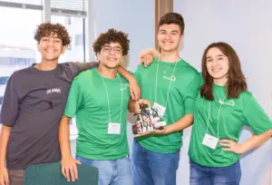 Students smiling at the camera. One of them is using a brown shirt and the other 3, a green one