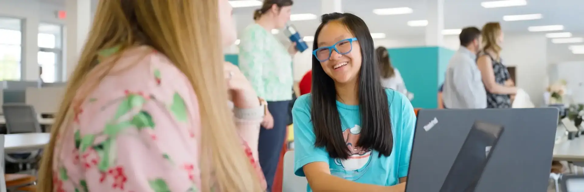 Student wearing a blue shirt and a blue pair of glasses talking with another female student